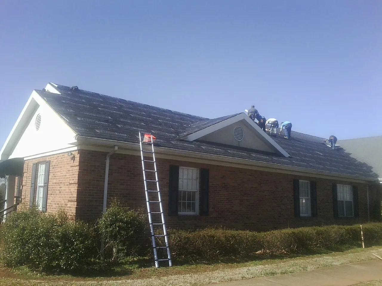 Crew tearing shingles off a brick ranch roof with a ladder set — Emergency Roof Repair work by our crew in Waucoma