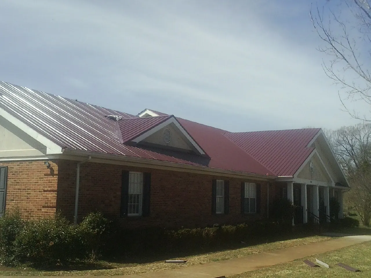 Red metal roof with gabled entries on a long brick building, from a Hail Damage Roof Repair job in Waucoma
