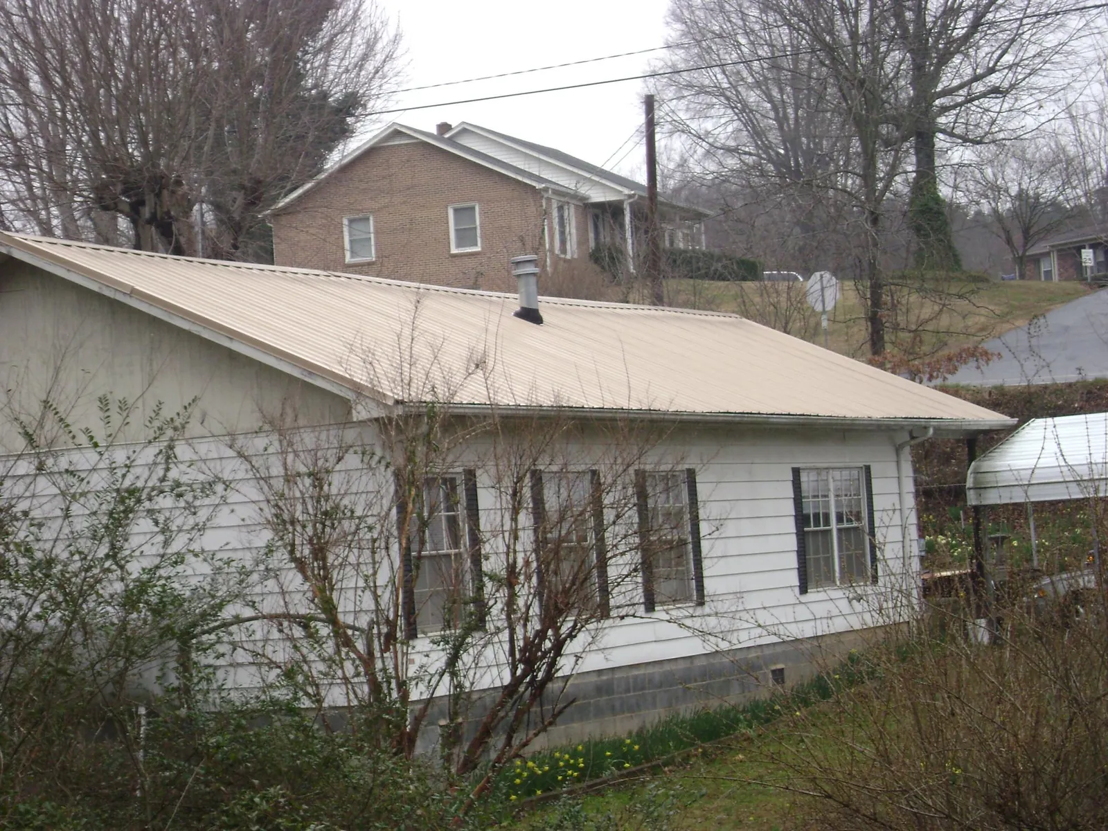 Tan metal roof on a white sided house set into a hillside — Commercial Roofing by Roofing Brothers in Waucoma